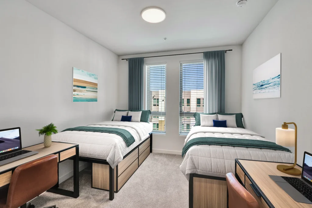 Living Room with desks, chair, laptop, beds, beach wall painting, and window with curtains in view.