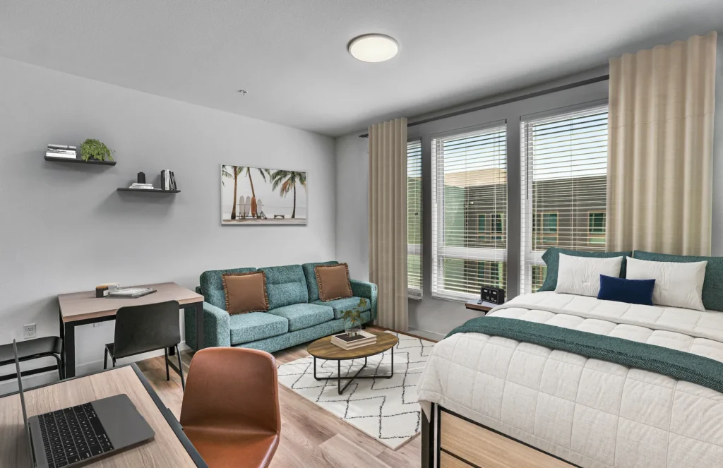Living Room with desks, chair, laptop, bed, tropical wall painting, and window with curtains in view.